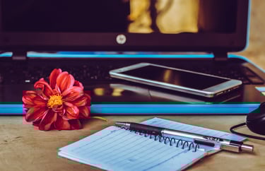 Téléphone portable posé sur le clavier d'un ordinateur avec un carnet, stylo et une fleur rouge posés à côté