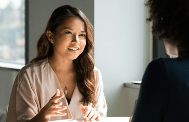 two women of color sitting at a table talking to each other
