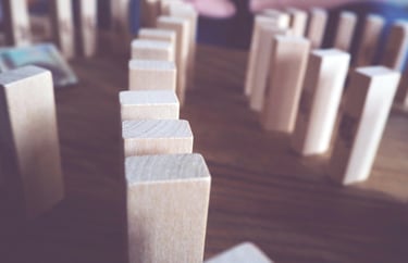 Close-up van houten blokken zoals domino, één valt om, symboliseert gevolgen in de praktijk.