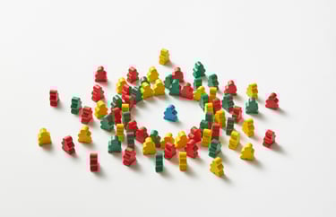 Houten poppetjes in verschillende kleuren rond een ander poppetje, symboliseert teamimpact/emoties.