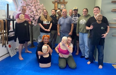 a group of smiling students in a dojo holding some of the training manikins 