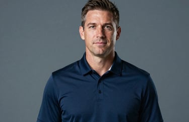 Studio portrait of a sports professional wearing a dark navy blue polo shirt with a subtle collar detail. Professional lighting, neutral gray-blue backdrop, North American / US Southern athletic director persona.