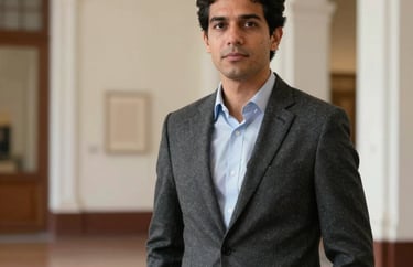 A portrait of a male lecturer in a sophisticated charcoal jacket, standing in a South American university gallery with off-white walls and architectural depth.