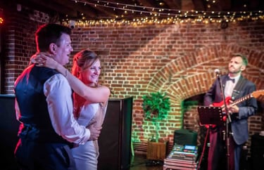 A happy bride and groom enjoy their first dance with a live wedding band in a rustic brick venue.
