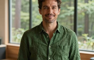 Portrait of a North American facilitator in a warm, sunlit studio with large windows overlooking a forest, wearing a moss green linen shirt, exuding a calm and compassionate expression.