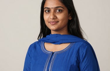 A professional studio portrait of a young South Asian female educator with a kind expression, wearing a vibrant blue traditional modern fusion outfit, off-white background, soft lighting.