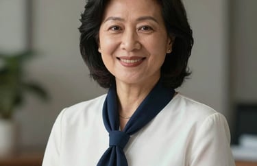 Professional portrait of a mature Southeast Asian woman in a white blouse and navy scarf, smiling warmly, corporate photography style.