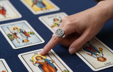 A high-quality photograph showing the detail of a silver ring with mystical symbols on a woman's hand as she points to a specific card on a Taro spread. Deep navy and pearl white tones dominate the frame.