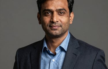 Professional studio portrait of a South Asian male executive in his 40s, wearing a steel blue shirt and dark blazer, neutral background.