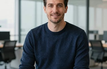 A professional headshot of a male career advisor in a dark blue sweater, sitting in a bright modern office with glass partitions.