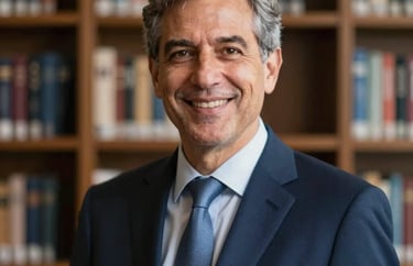 A professional portrait of an academic leader in a dark blue business suit, smiling confidently in front of a blurred bookshelf background. North American / International professional style.
