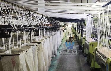 Industrial textile machinery in a zipper manufacturing plant is weaving white fabric yarn.