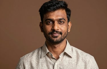 Portrait of a South Asian / Indian man with a professional demeanor, wearing a light-colored linen shirt, set against a warm earth-toned background.