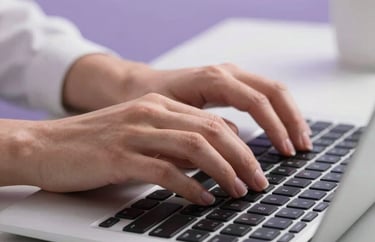 Close-up of hands typing on a modern keyboard in a clean, professional North American office environment. The surrounding space has soft lavender accents.