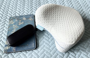 Knee pillow resting on a neatly made bed beside an iPad and reading glasses for bedtime comfort