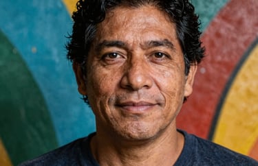 A professional South American / Brazilian Amazonian close-up portrait of a male theater director in a square crop. Expressive, friendly face, with a colorful painted wall behind him.