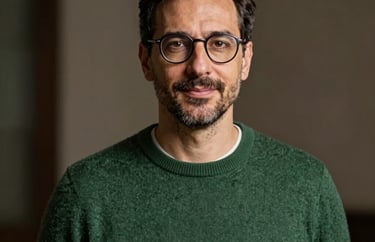 Portrait of a professional man in his 40s with glasses and a soft forest green sweater, Southern European / Italian background, elegant and approachable.