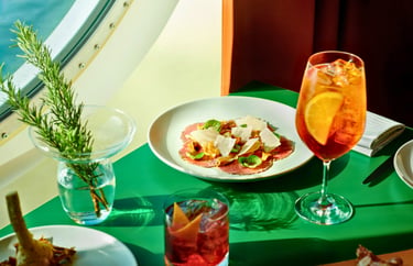 Italian beef carpaccio with parmesan cheese served alongside an Aperol Spritz cocktail on a green table.