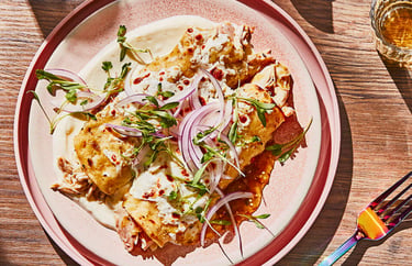 Shredded chicken enchiladas suizas topped with white cream sauce, red onions, and fresh cilantro.