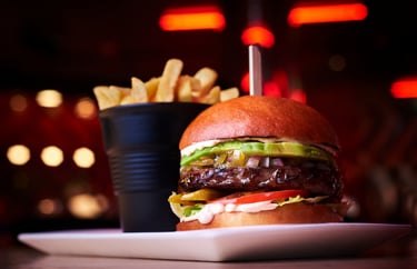 Gourmet beef burger with avocado, pickles, and red onion served with a side of crispy golden fries.
