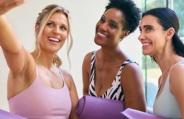 Three diverse women in athletic wear smiling for a selfie after a yoga workout.