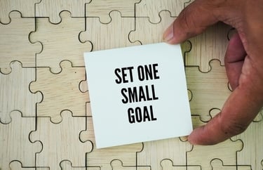 Hand placing a motivational note saying Set One Small Goal on a wooden jigsaw puzzle.