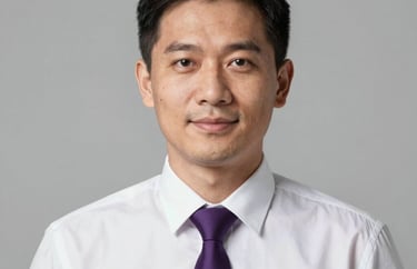 Professional studio portrait of a Southeast Asian man in a white formal shirt and purple tie, looking professional and friendly. Neutral light grey background.