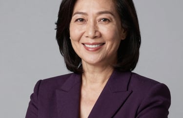 Professional studio portrait of a Southeast Asian woman in her 40s wearing a dark purple blazer, looking confident and smiling warmly. Neutral light grey background.