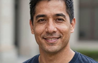 Professional headshot of a North American man with a friendly, intelligent expression. Natural outdoor lighting with a blurred architectural background.