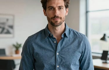 A professional portrait of a man in a muted blue shirt, looking confident in a bright, modern creative studio. North American / US professional setting.