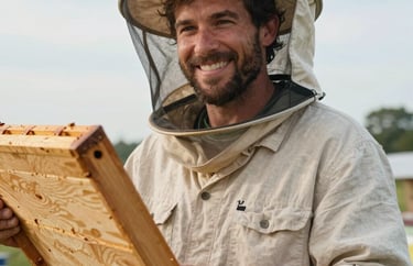 A portrait of a male head beekeeper smiling warmly outdoors at a North American / US farm, wearing a light beige linen shirt and holding a wooden hive frame.
