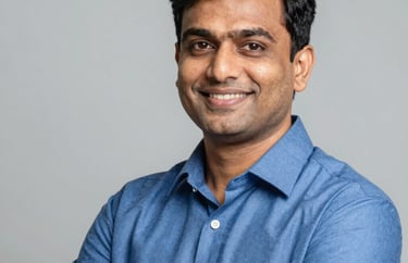 A professional portrait of a South Asian male educator in a smart blue shirt, smiling with a sense of purpose against a clean, premium background.