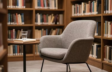 A quiet corner of a modern South American library with a single designer chair and a small side table holding a glass of water and a book. Calm, sophisticated mood.