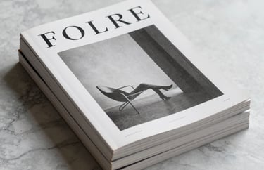 Minimalist photography of a stack of literary magazines on a marble surface. The covers feature clean typography and artistic black and white photography. Soft, elegant studio lighting.