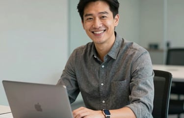 Portrait of a smiling professional in business casual attire sitting at a clean, white conference table with a laptop. Professional setting, North American / US.