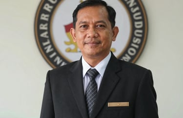 Professional portrait of a male Indonesian school principal in formal attire, standing in front of the school's logo, professional and welcoming expression.