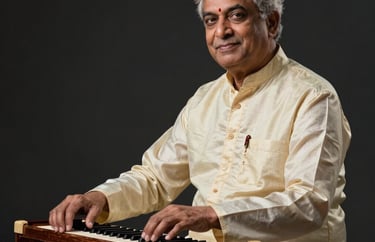 Professional studio portrait of a senior South Asian / Indian male music maestro in a traditional cream silk outfit, sitting with a harmonium, cinematic low-key lighting in a charcoal black setting.