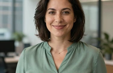 A professional headshot of a person in a sage green blouse, with a soft, confident smile, set in a North American urban office setting.