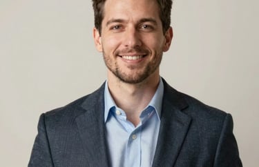 A studio portrait of a male professional in the North American philanthropic sector, dressed in business casual attire with a warm, confident expression. Neutral off-white background with soft, elegant lighting.