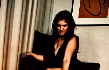 Coralyn wearing black dress posing on recliner chair.