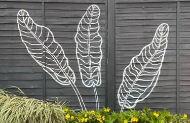 Three large banana leaves painted in a modern graphic style on a grey yard fence and flowers.