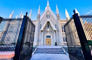 Gothic-style stone assembly hall with white spires behind a wide open black wrought iron gate.