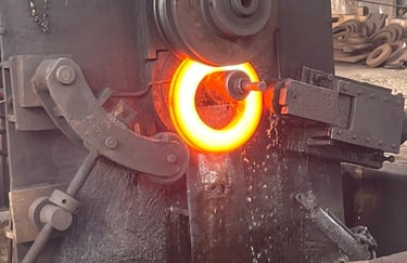 Industrial ring rolling machine shaping a glowing red-hot metal ring in a steel forging factory.