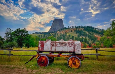 Rustic vintage water wagon in a field with Devils Tower National Monument in the background under a dramatic sky.