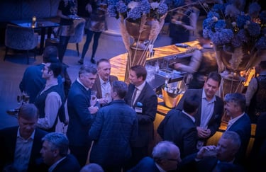 Business professionals networking at a sophisticated cocktail event with blue flowers and an elegant bar.