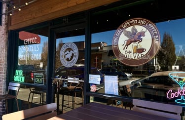 Storefront of Flying Bull Taproom and Coffee Bar with cafe seating and neon signs for craft beer and cocktails.