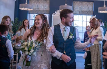 Smiling bride and groom walking down the aisle after an indoor wedding ceremony with guests.