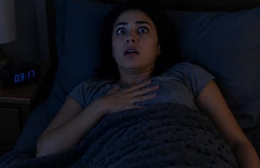A startled woman waking up with a shocked expression in a dark bedroom at night.