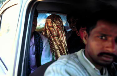 A crowded interior view of a car featuring a bride in a shimmering gold veil and other passengers looking at the camera.