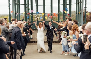 Bride and groom walking through confetti time and laughing with their hands up